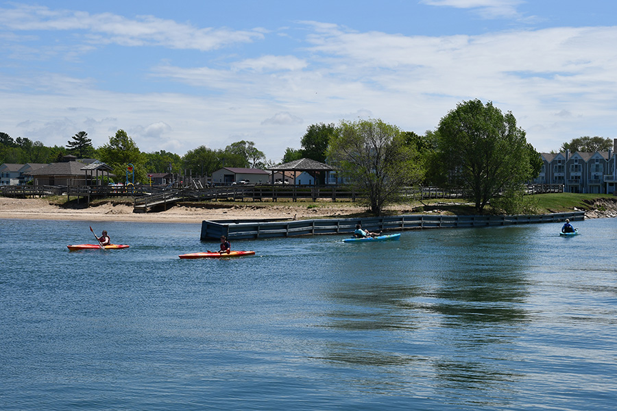 People in kayaks on a lake with beach and park behind.
